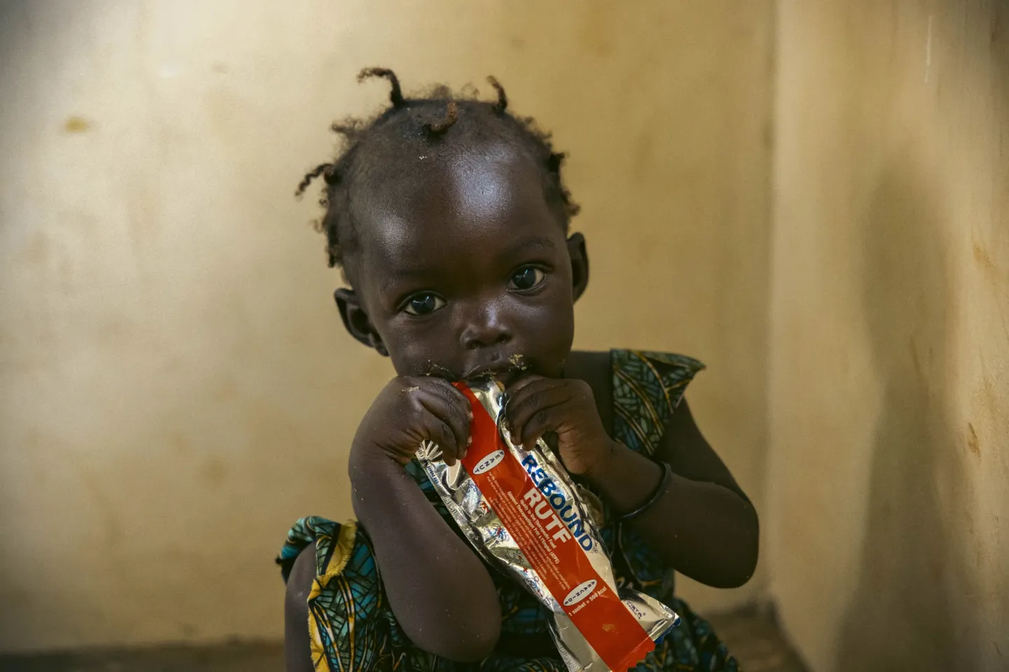 One-year-old Brenda eats from a sachet of Ready-to-Use Therapeutic Food (RUTF) after her nutrition assessment at Uriama Health Centre III in Terego District, Uganda.