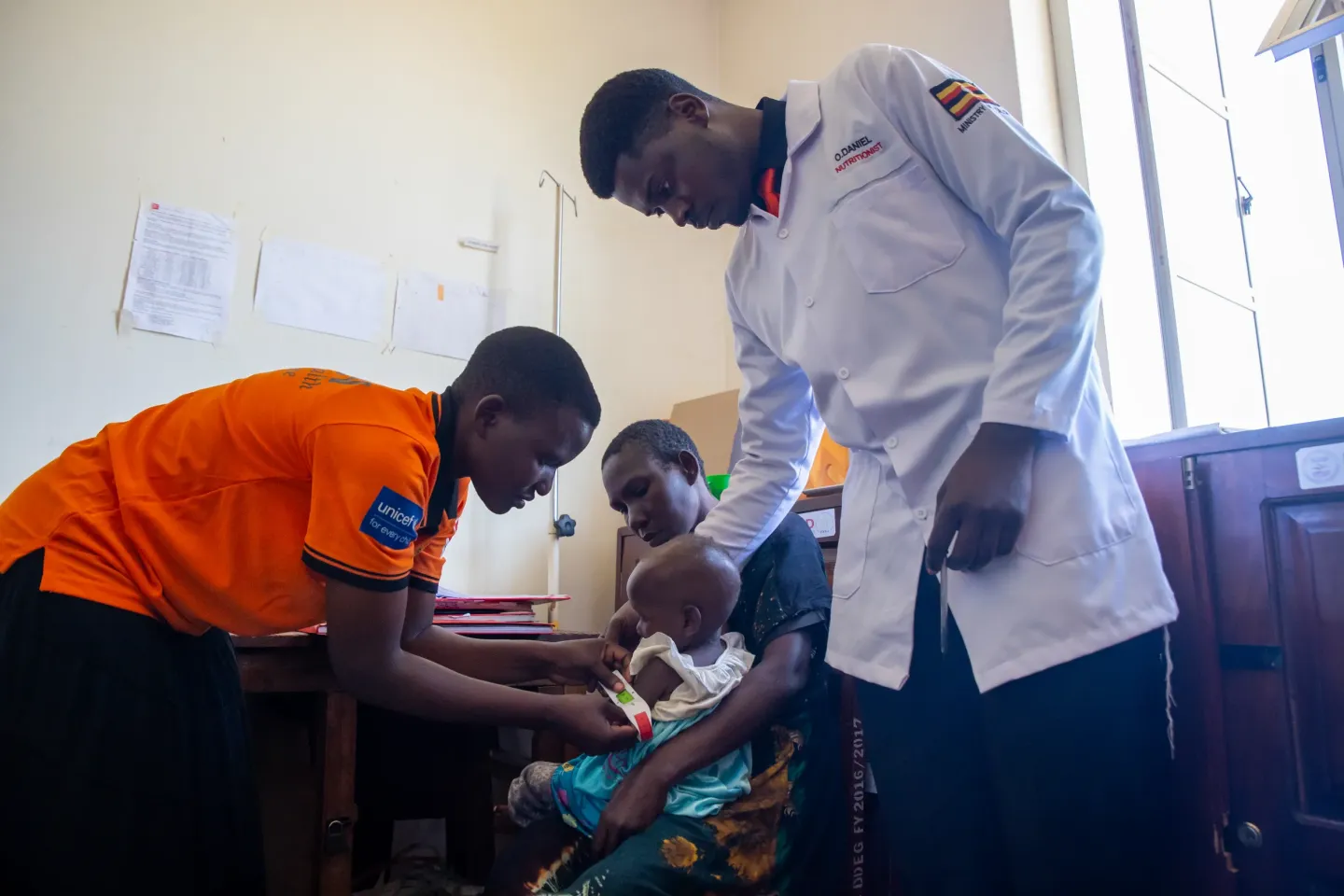 Supervised by Nutritionist Daniel Ombada at Masafu General Hospital in Busia District, Christine Amojong, a Community Health Extension Worker takes the Mid-Upper arm Circumference (MUAC) measurement of Grace Nabwire's daughter, one of the active referrals by the Community Health Extension Workers programme.