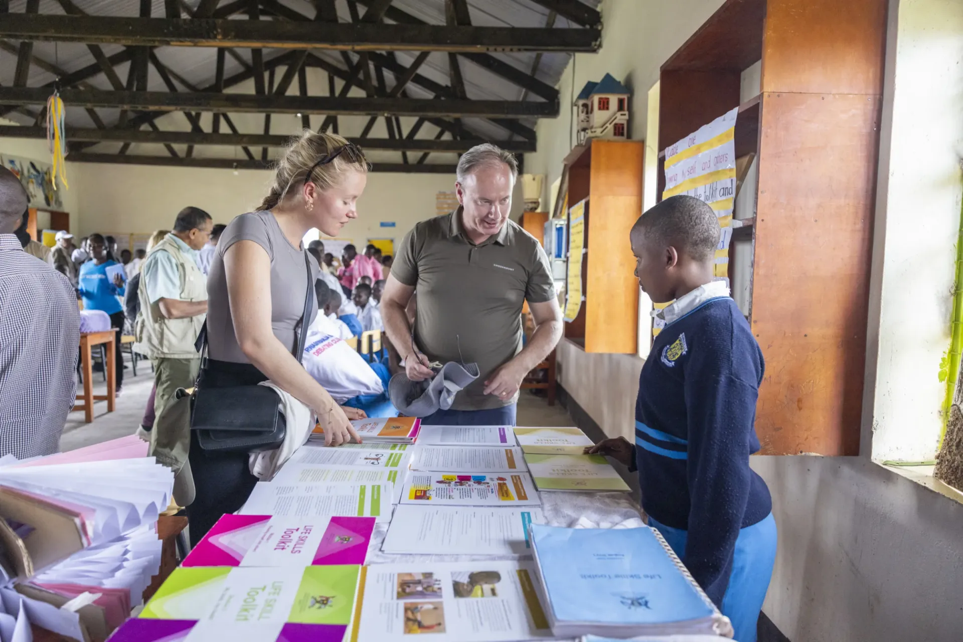 Maja Kajsjo Mikkonen from the Embassy of Sweden and Magnus Berntsson, Swedish Member of Parliament (Christian Democrats), interact with Keria Akeza, a refugee student at Rwamwanja Secondary School in Kamwenge District, as she showcases different Life Skills toolkits displayed on a table, part of the UNICEF-supported Life Skills Club.