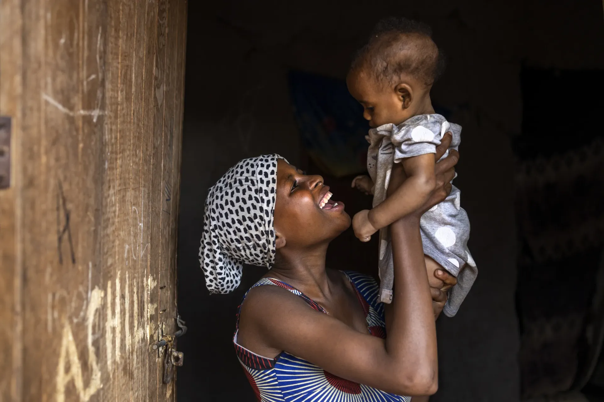 Here's the text formatted for easy copying: Janine Mafie, 15, poses with her baby at their home in Kyangwali Refugee Settlement, Kikuube District, western Uganda, on July 16, 2025. Having arrived at the settlement alone and pregnant, Janine now receives support through a programme that combines cash assistance, mentorship, and access to healthcare&mdash;helping her rebuild her life and care for her child.