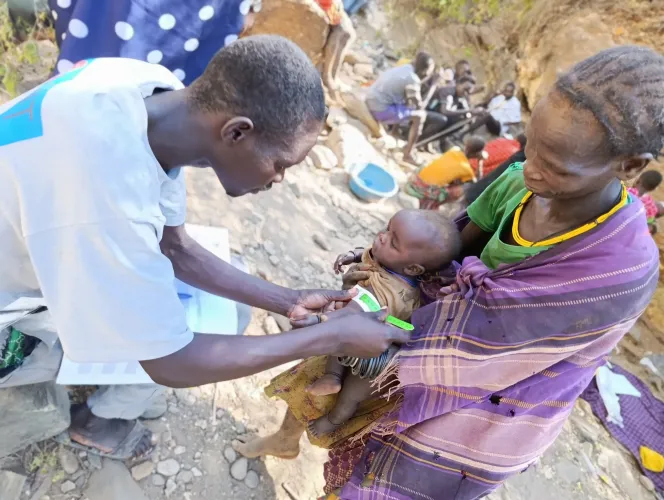 On 17 June 2026, a health worker from Kakingol Health Centre III uses a mid-upper arm circumference (MUAC) tape to screen Adong's youngest son for malnutrition at a gold mining site in Katikekile Sub-County, Moroto District, Karamoja, Uganda. 
