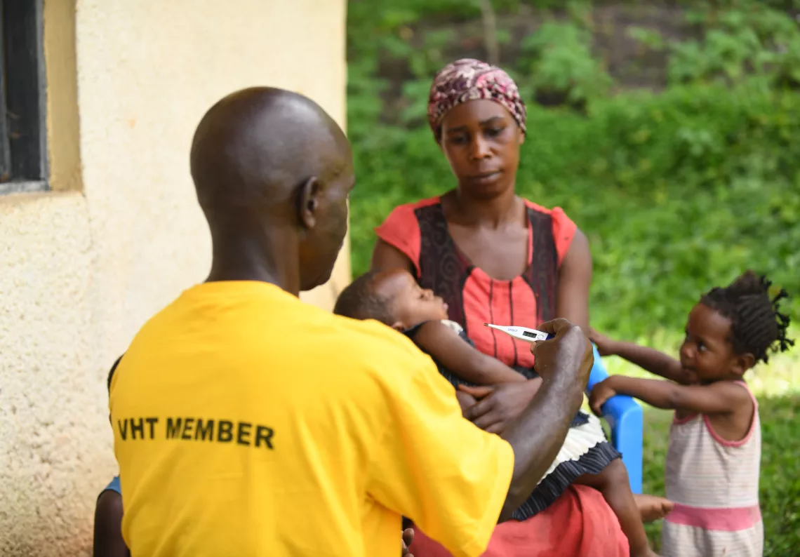 Bazimbana Fenehasi, a UNICEF trained Village Health Team member takes the temperature of a one-year Namakula Abigail as her mother Nakachwa Justine carries her. High fever is one of the symptoms of malaria.  This was during Bazimbana routine checks on homes in Kabingo village in Ntungamo district. UNICEF trained VHTs to handle malaria among children under five years in Ntungamo district. He said that he routinely moves door to door to deliver health services including health education on how to prevent mala