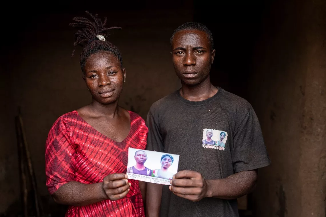 Muhindo Jovia Duduma (left) and her brother, Jockim Duduma, stand in the doorway holding a photo of their parents who were killed during an attack by armed groups on their community in June 2023.