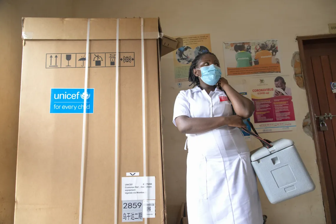Racheal Kiconco, a nurse at Kamwenge District Health Centre, operating as a health worker in charge of COVID-19 vaccination in Rwamwanja Refugee Settlement, Kamwenge District, gets ready to move with her vaccine carrier to carry on her duties. On the right is a newly donated fridge from UNICEF which will be used to support the cold chain system at the health center. 