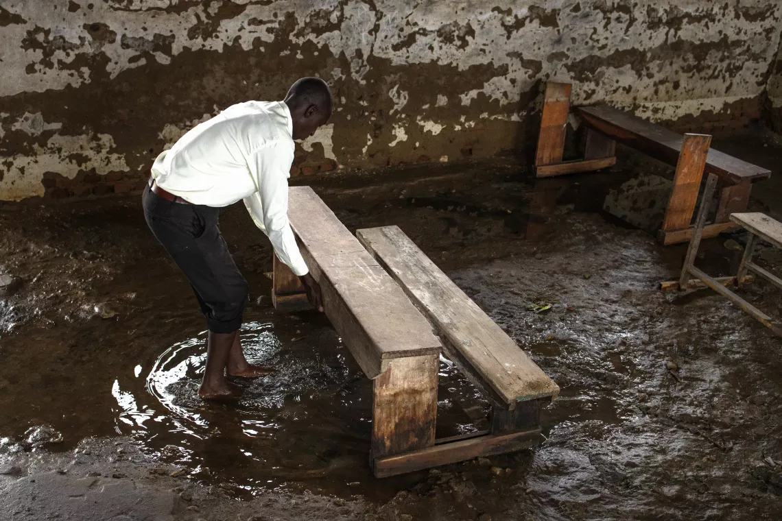 Vicent Asiimwe, the Head Teacher of Masaka Primary School in Butungama Sub-county, Ntoroko District, tries to organize the classroom furniture, stacking it in one place amidst the waterlogged floors and stained walls on September 4, 2024. 