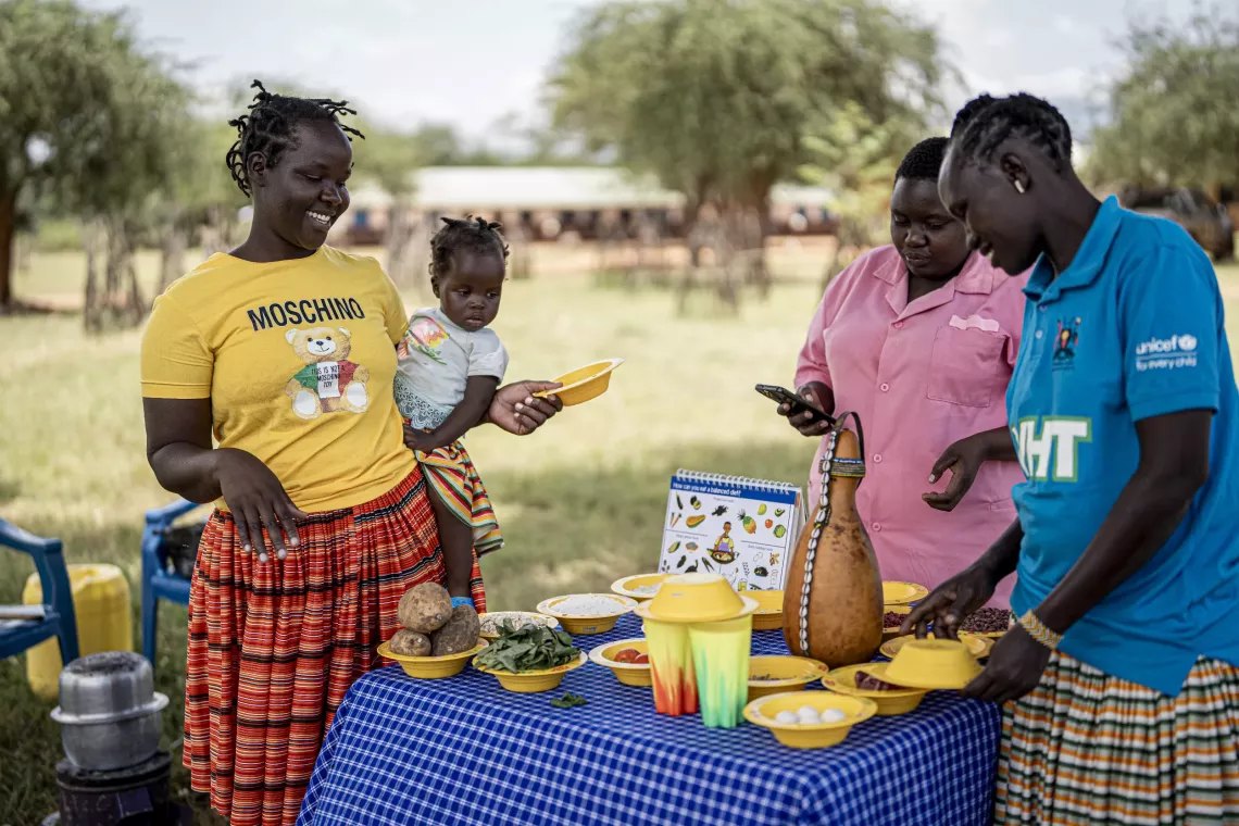 Apoa Gloria (middle), the nutrition focal person at Loroo Health Centre, and VHT Chepkasi Lena, demonstrate food preparation using locally available foods to mothers and caregivers at an Early Childhood Development centre in Loroo, Amudat District.