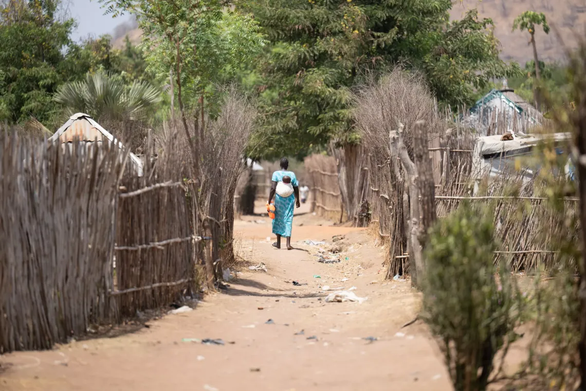Atoch Riak walking back home after a training with other care group mothers on nutrition and feeding for children at Nyumanzi refugee settlement.