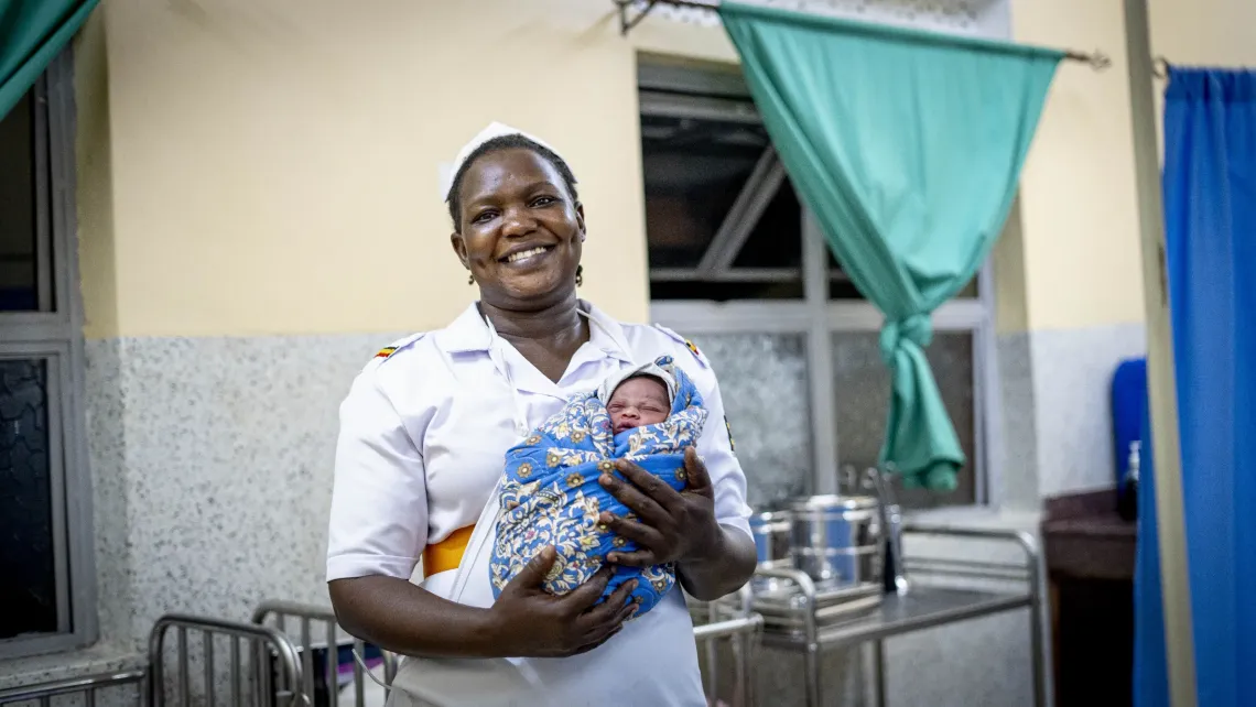 Midwife Sharon Akullo holding a newborn in the labour suite at night at Amomwa Health Centre III Dokolo district. She remembers using a torch for deliveries, as poor lighting made procedures risky. New solar lighting has improved night shift safety and maternal care. 
