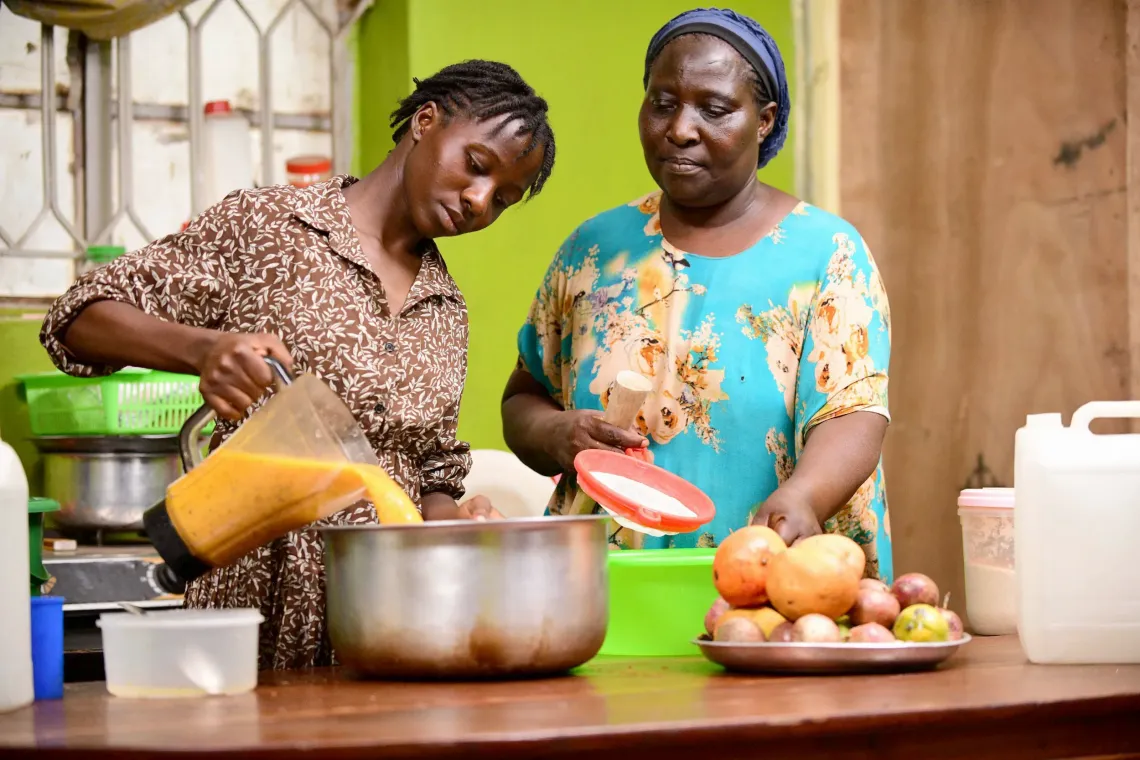 (L-R) Ndibalekera Maria Judith, one of the beneficiaries of the Girls Empowering Girls program, with her mother, Doola Nassimu, makes fresh juice for their small fresh juice business at their home in Kisenyi Zone in Kampala.