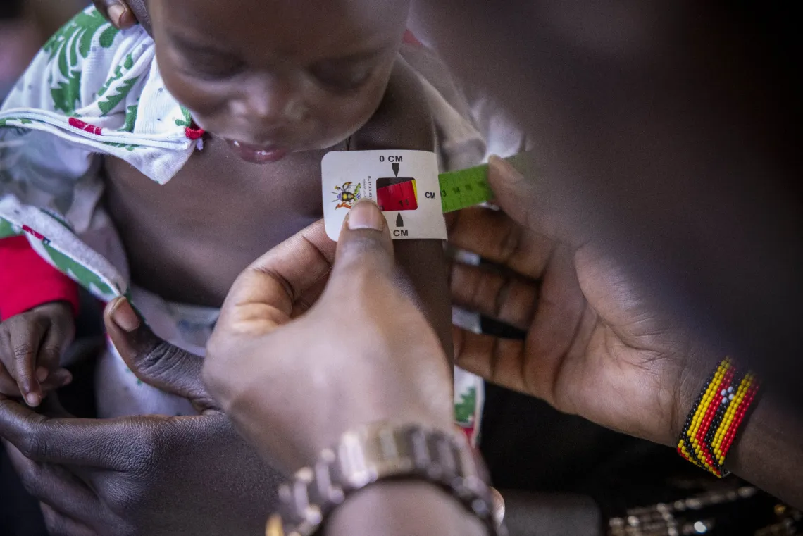 A mid-upper arm circumference (MUAC) tape is used to assess a child during a nutrition screening at Uriama Health Centre III in Terego District. Early screening helps identify children with severe acute malnutrition and connect them to treatment before their condition worsens.