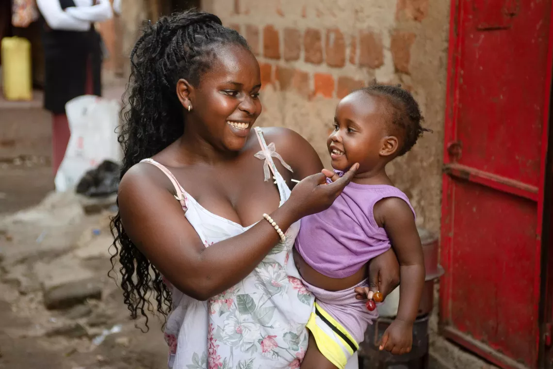 Esther Wema, 16, a teenage mother, enjoys a light moment with her two-year-old daughter Amira Jemima outside her rented one-room house in Katanga Kampala, Uganda.