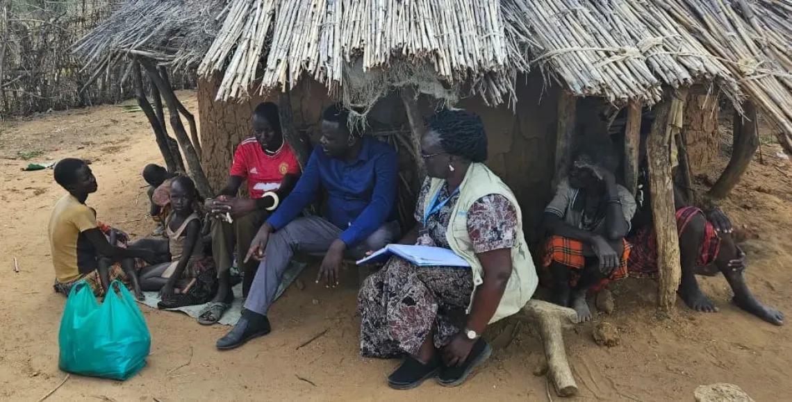 Veronica Nachan, seated right, sits with her youngest child outside her home in Nakapelimoru Sub-county, Kotido District, during a community outreach visit by district health officials, a Village Health Team member and UNICEF.