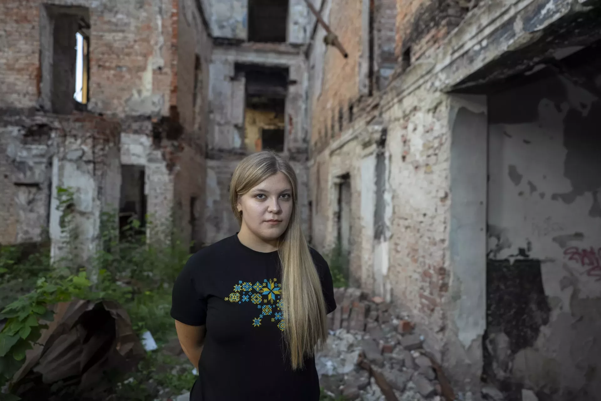 17-year-old Sofiia from Kharkiv stands against the backdrop of a wall destroyed by shelling