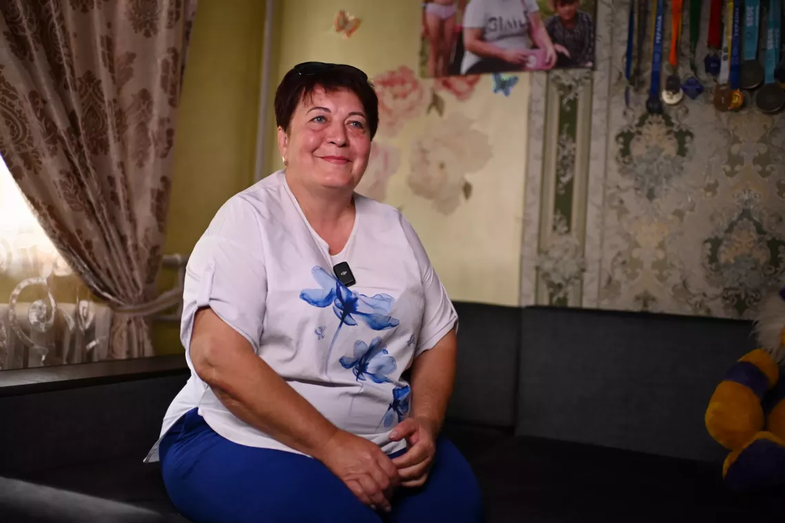 Жінка у білій футболці із блакитними квітами сидить на дивані в кімнаті