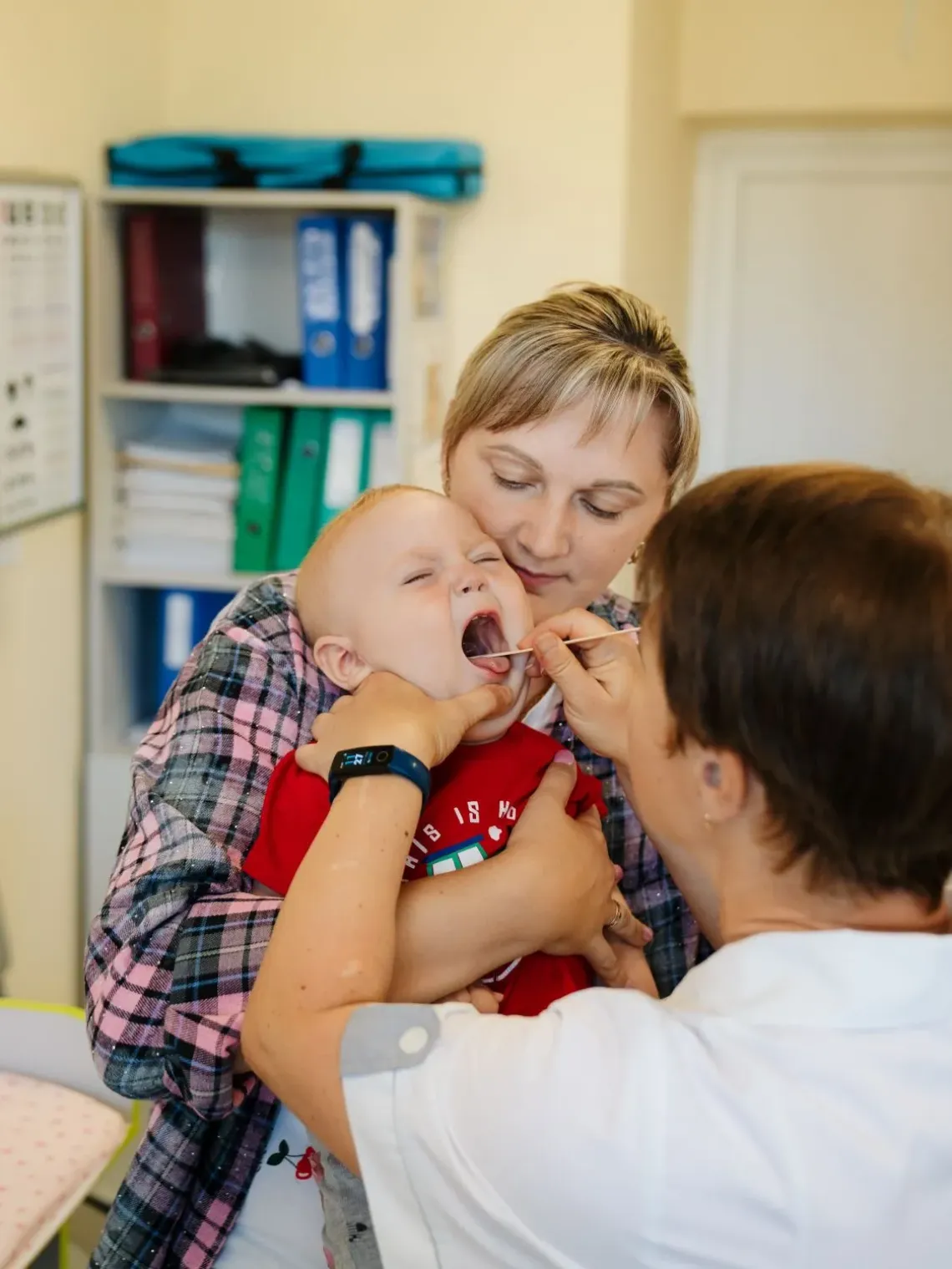 A doctor is checking on the baby boy while his mom is holding the child.