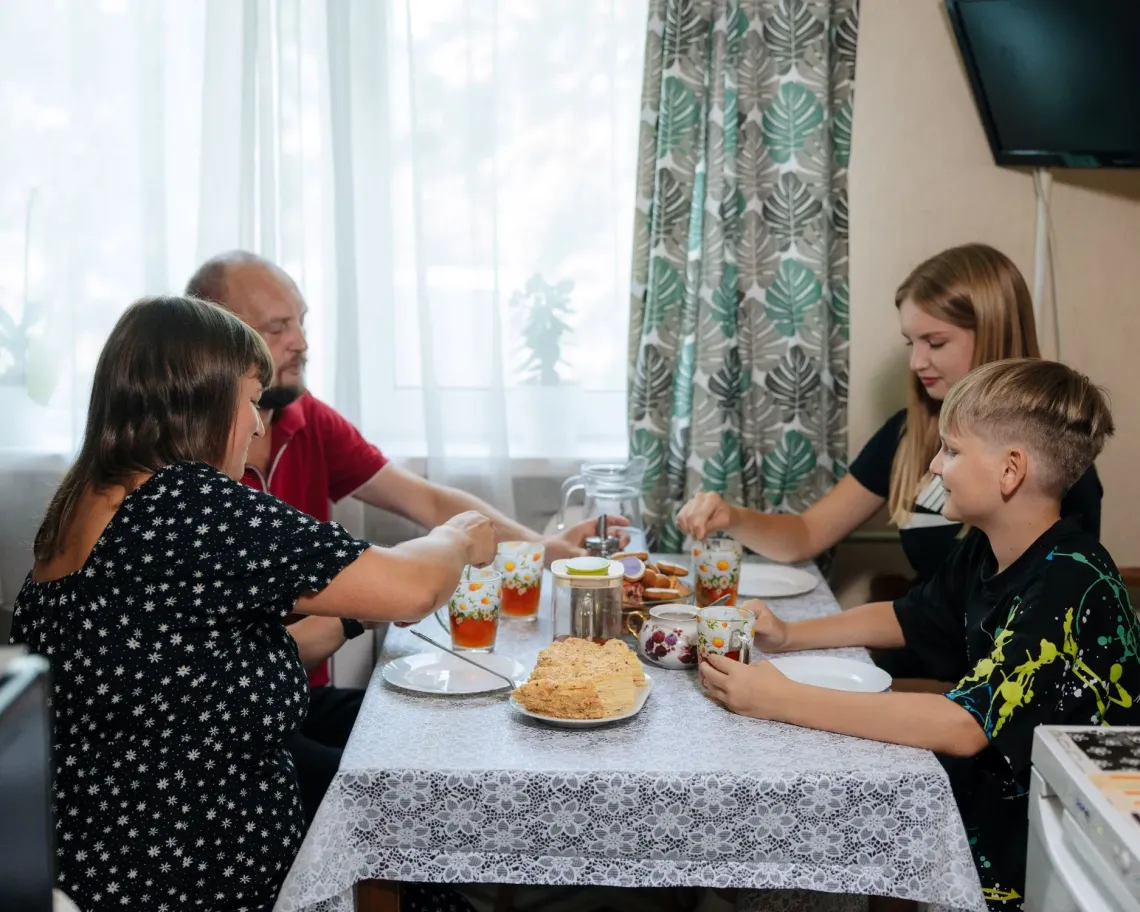 Parents and two children are sitting in the kitchen drinking tea