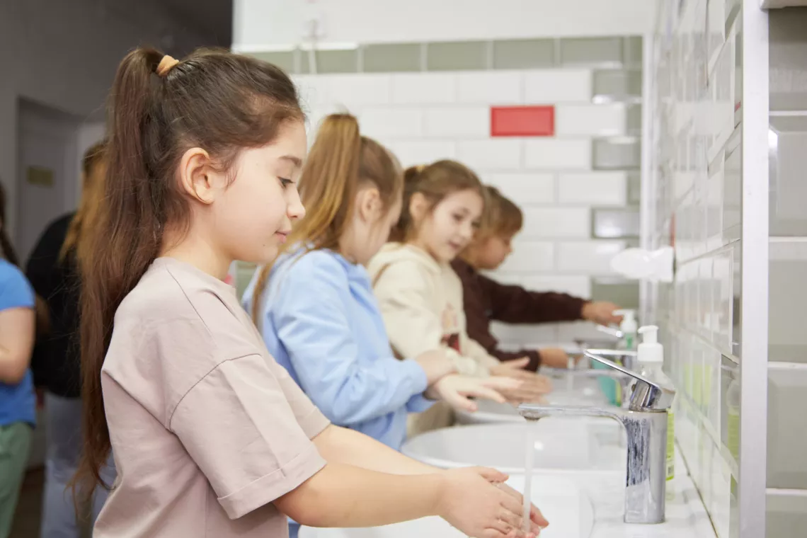 Учні і учениці молодших класів миють руки перед обідом у їдальні