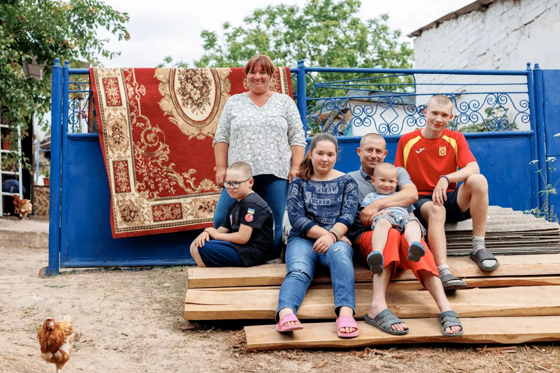 The family raises four children of their own. In the photo, they are at the gate of the yard, where they live as a large family. The war prompted them to become a foster family.