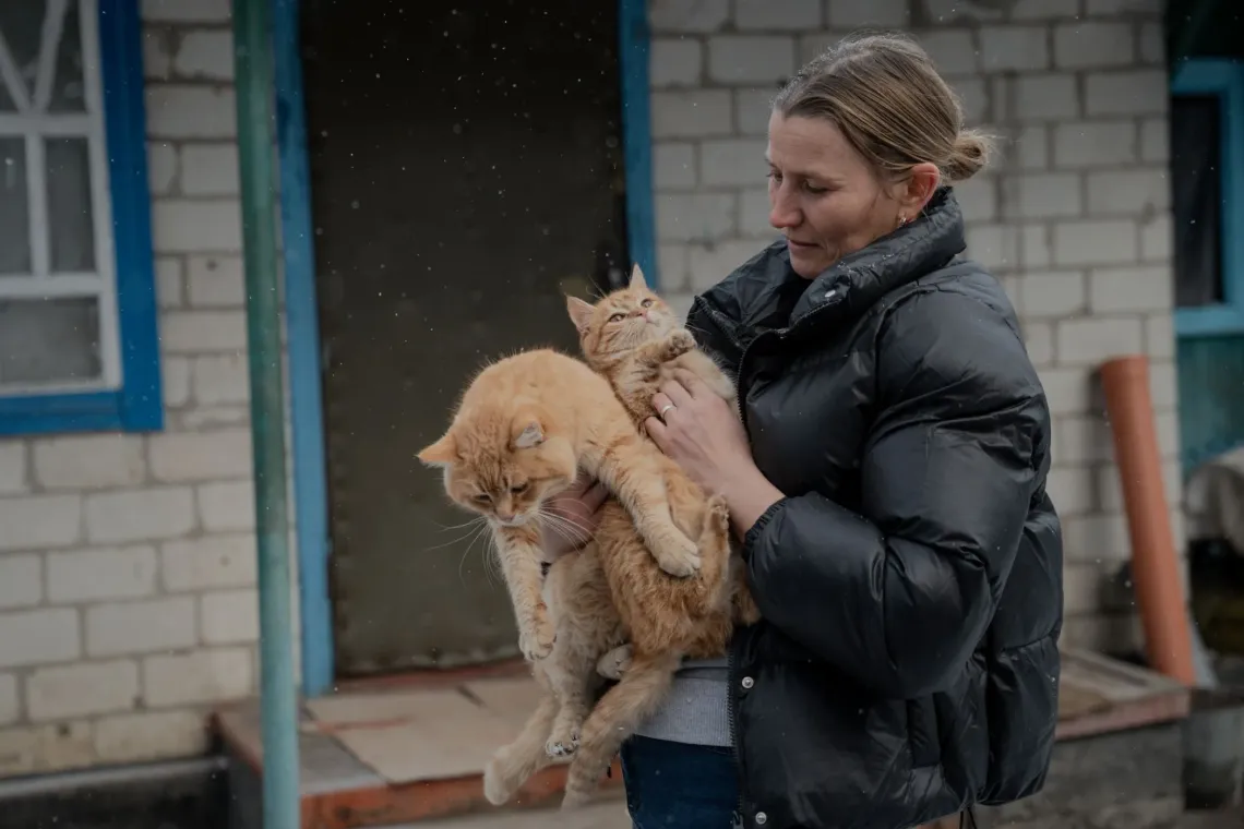 A woman holding a kitten stands near her private house in eastern Ukraine