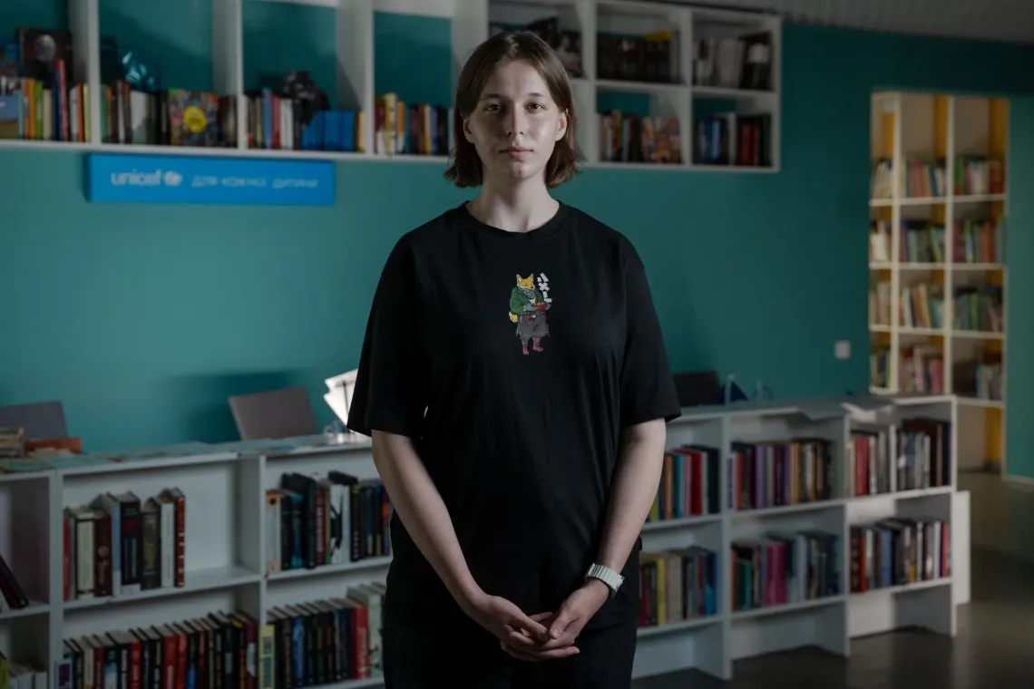 Facilitator of a youth club in Kharkiv standing among the book shelves.