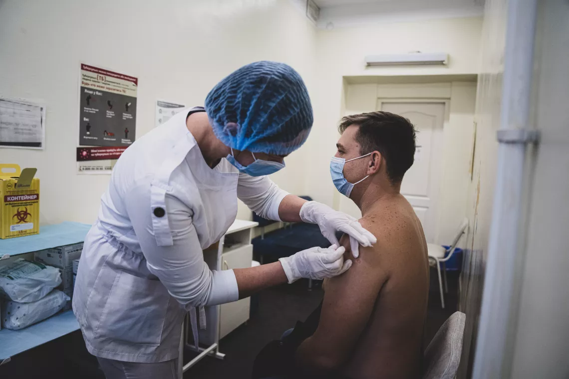 Пандемія COVID-19 в Україні. Медсестра робить щеплення чоловіку.