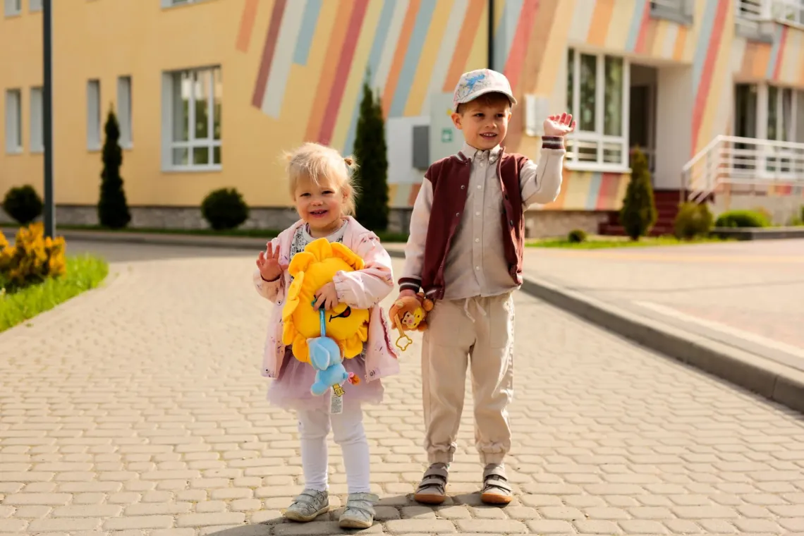 Two children standing near their kindergarten
