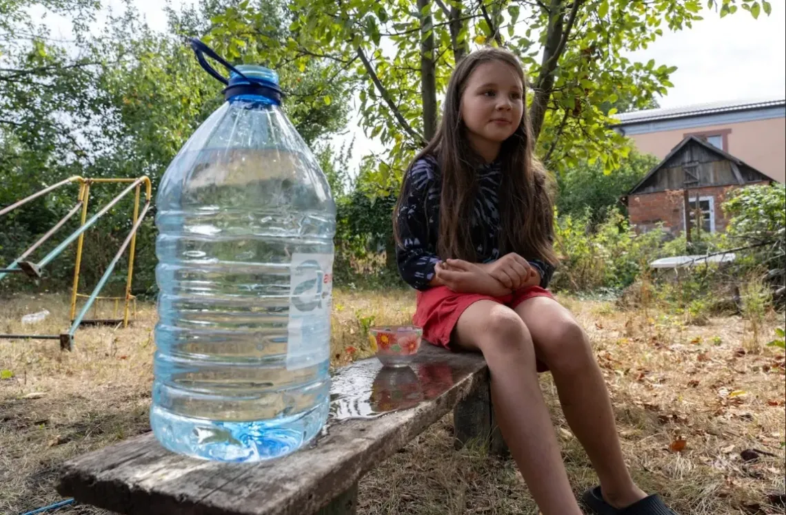 Girls sits on the bench near a jar of water. Sloviansk, Ukraine