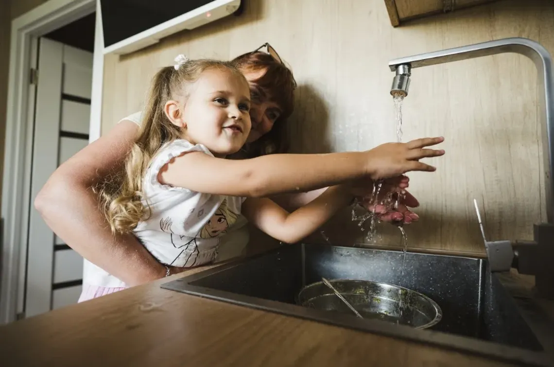 Woman holds her daughter while she is washing hands. Sumy, Ukraine