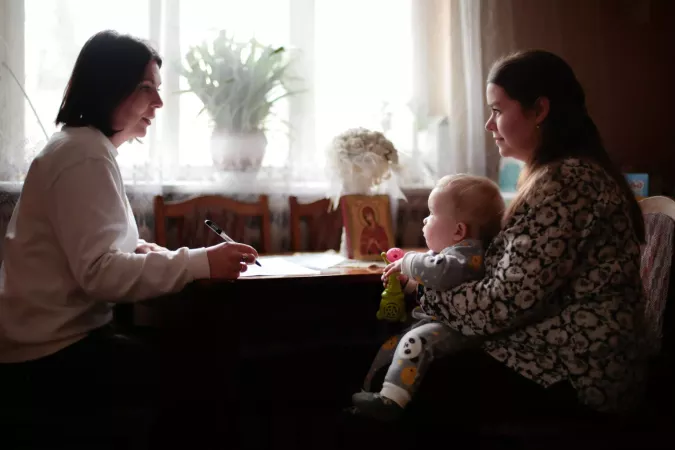 A nurse sits at a table next to a mother holding a baby