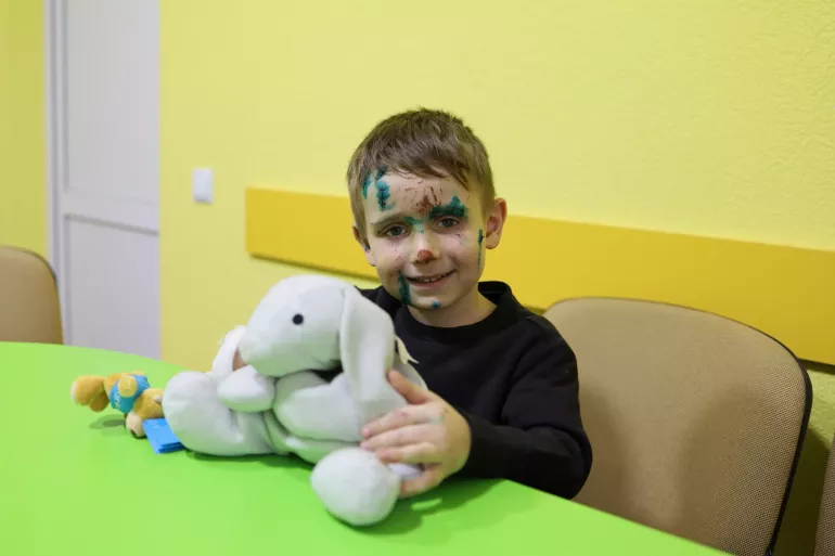 Emik holds a stuffed bunny. The boy's face shows wounds from the shelling of city Sumy.