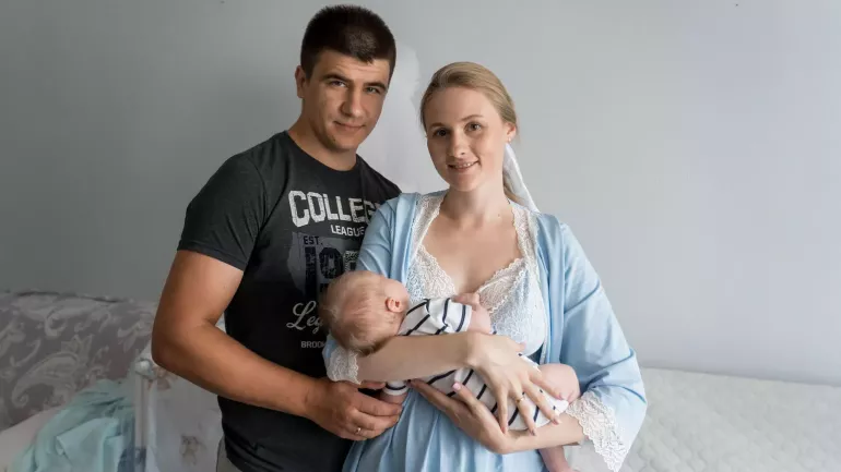 Чоловік стоїть біля жінки, яка тримає на руках немовля