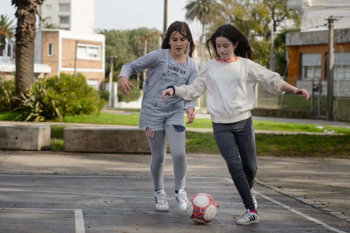 Dos adolescentes mujeres jugando al f&uacute;tbol en una plaza.