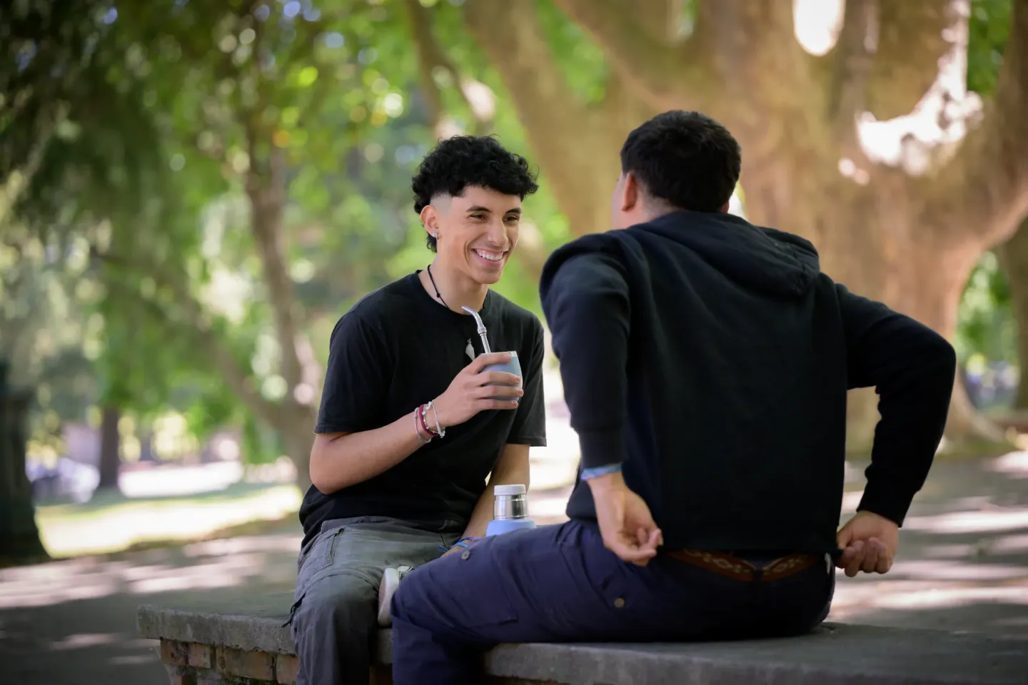 Dos varones sentados afuera, compartiendo un mate y conversando.