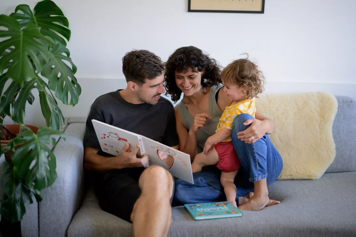 Padre, madre e hija sentados en el sill&oacute;n, leyendo un libro