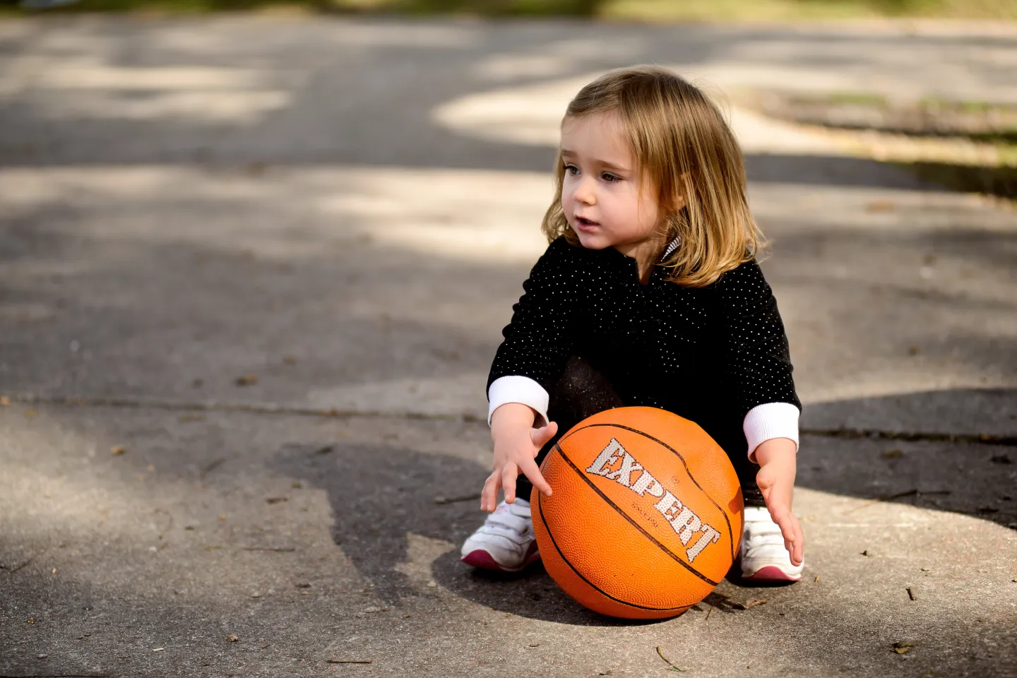 Ni&ntilde;a de unos dos a&ntilde;os, sentada en el piso, con una pelota de b&aacute;squetbol.