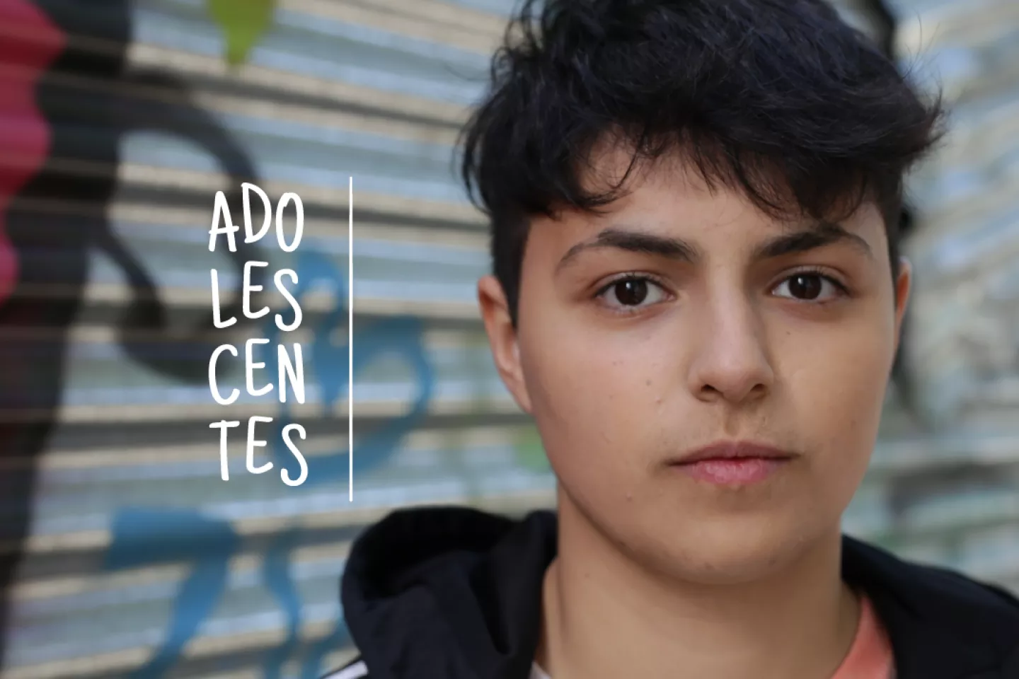 Adolescente var&oacute;n mira a c&aacute;mara, con chapa grafiteada de fondo