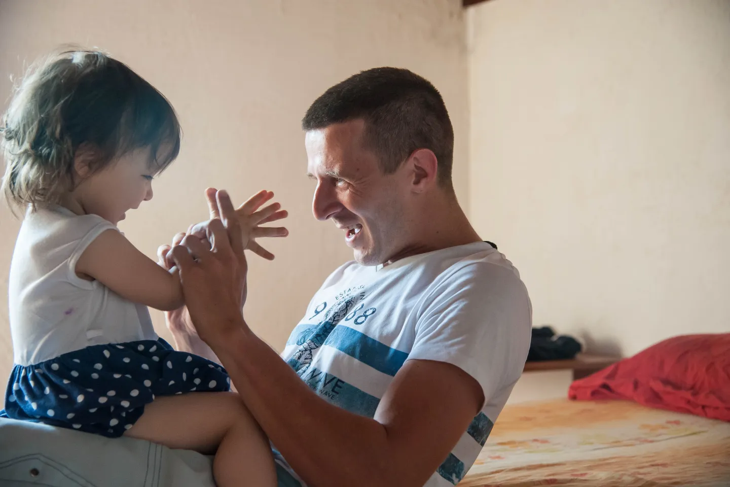 Padre, jugando con las manos de su hija, sentada en su falda, enfrentada hacia &eacute;l.