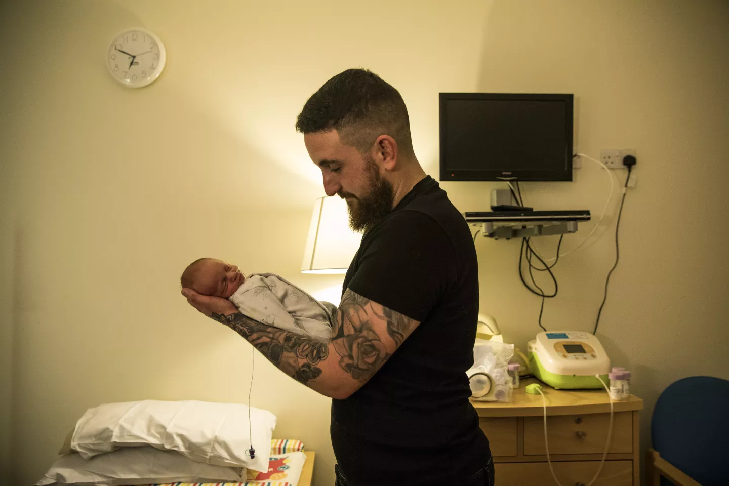 Hombre sosteniendo a beb&eacute; reci&eacute;n nacido, en habitaci&oacute;n de hospital.