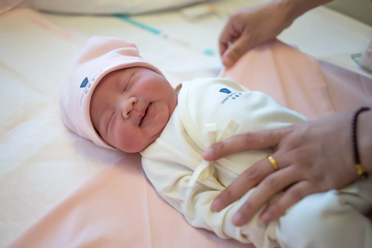 Beb&eacute; reci&eacute;n nacida, de gorro y enterito, con la mano de un adulto sosteniendo con protecci&oacute;n.
