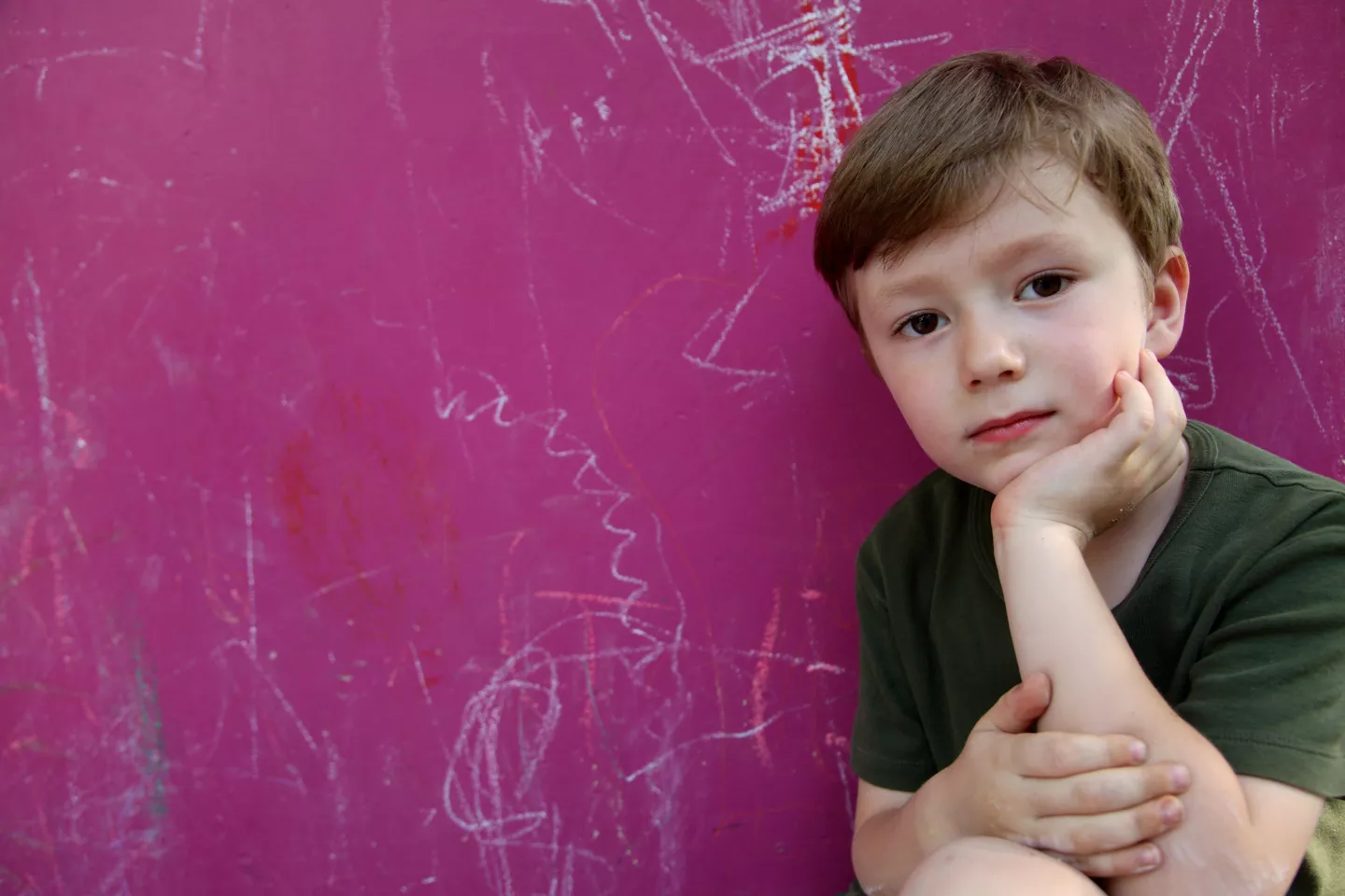 Ni&ntilde;o con el ment&oacute;n apoyado sobre su mano, mirando a c&aacute;mara. Detr&aacute;s de &eacute;l, una pared fucsia.