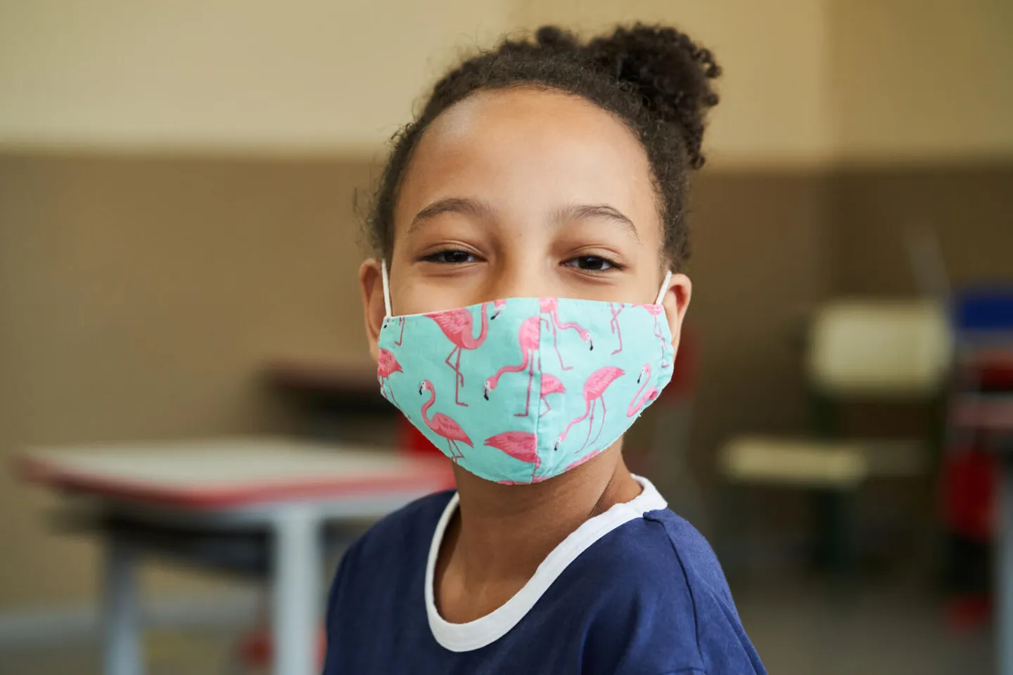 Primer plano de ni&ntilde;a con tapabocas de flamencos, sonriendo a c&aacute;mara.
