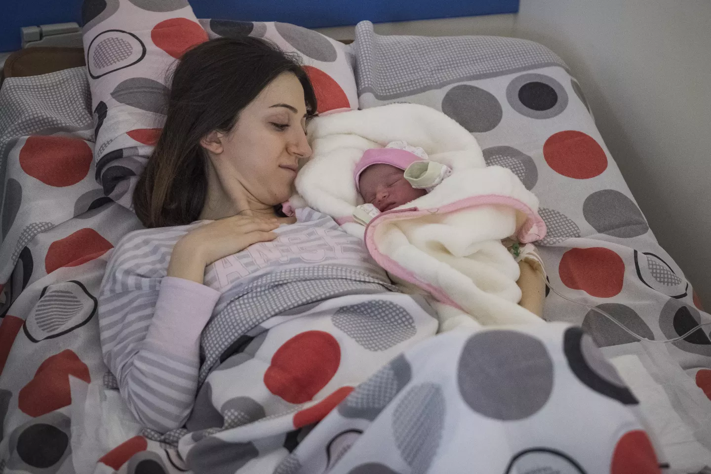 Mujer, acostada en una cama, abrazando a beb&eacute; reci&eacute;n nacido, a su lado.