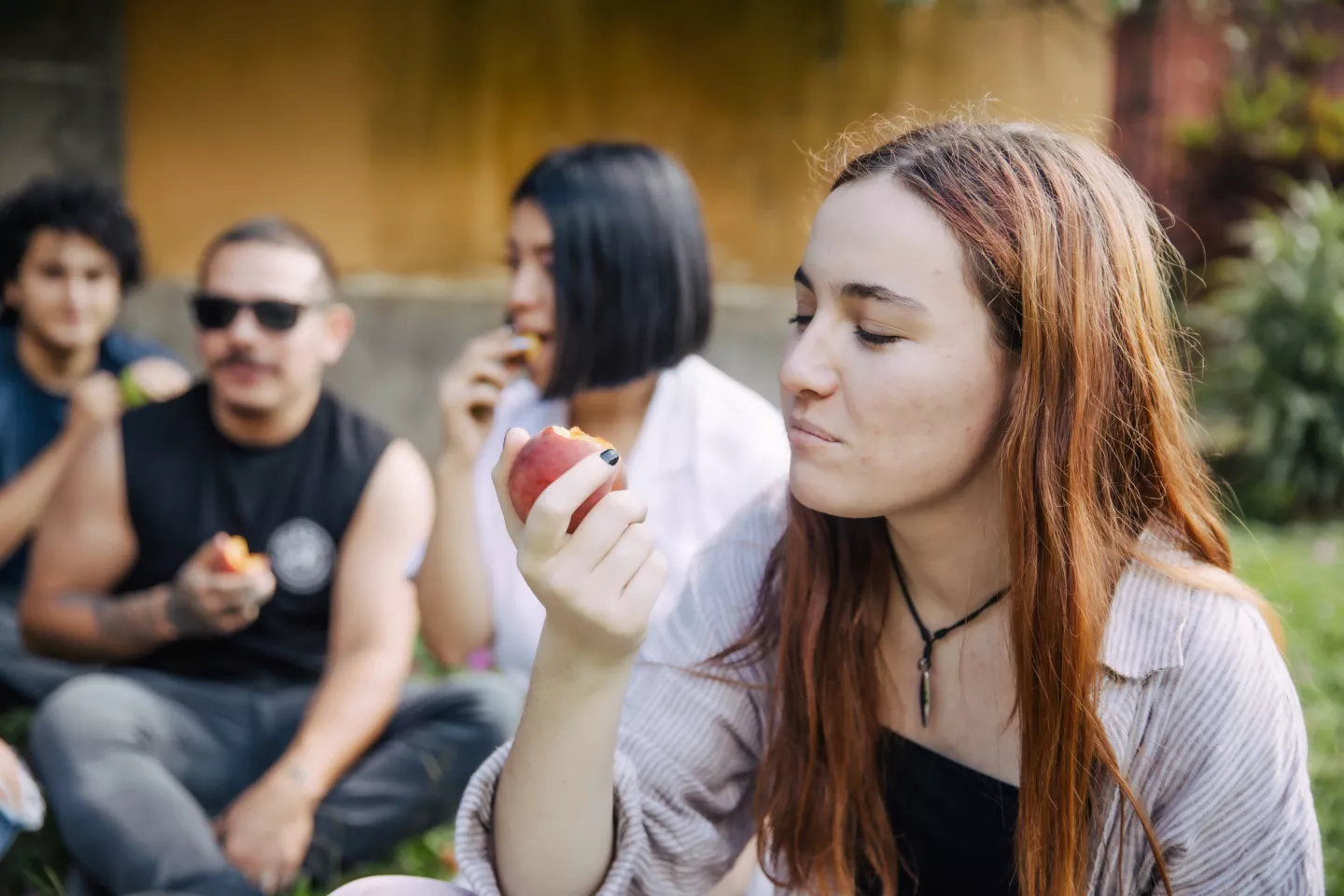 Adolescente mujer, comiendo manzana. Atr&aacute;s, se ven otros j&oacute;venes.