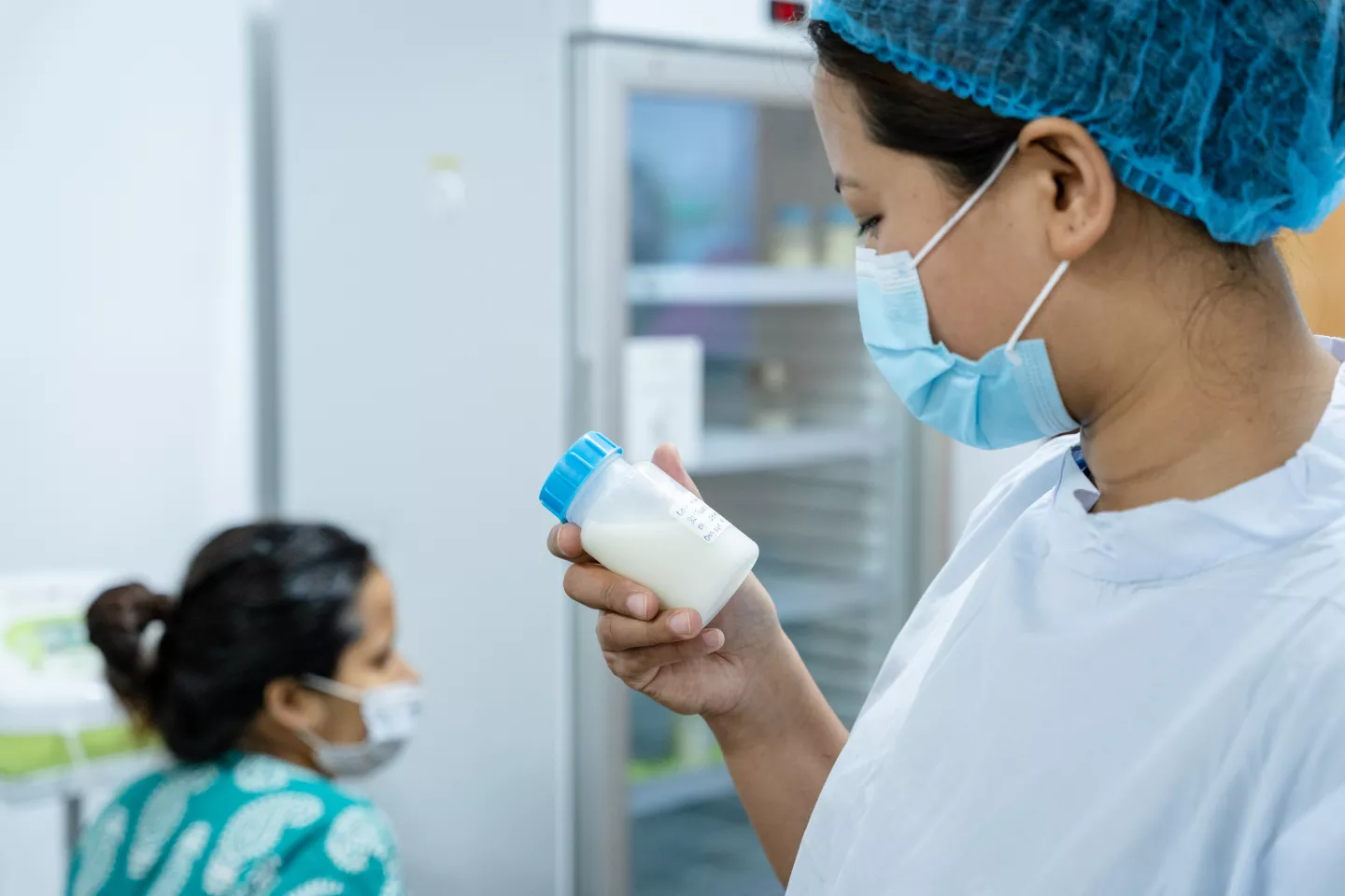 Mujer de gorra y tapabocas leyendo la etiqueta en un frasco de leche materna.