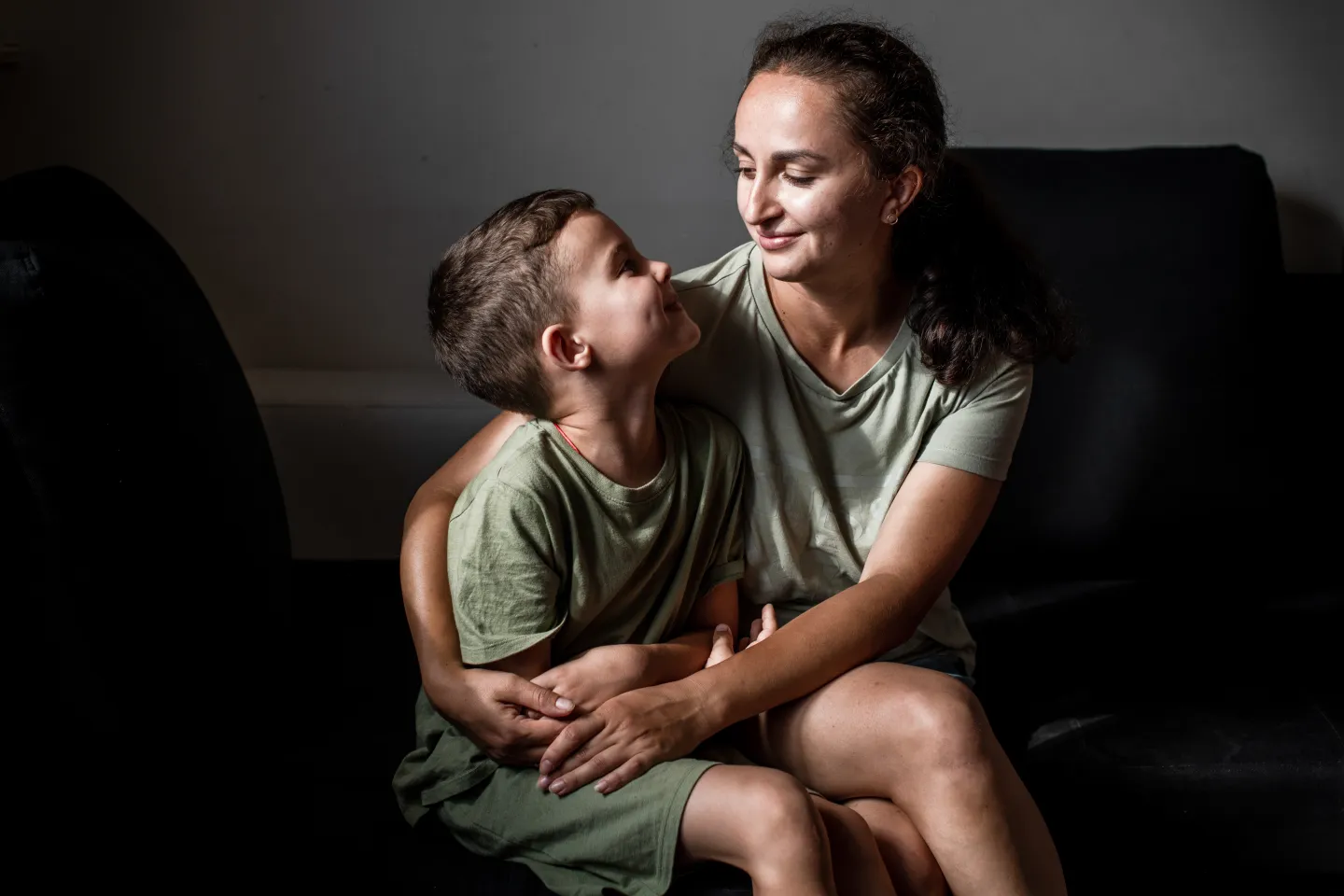 Mujer y ni&ntilde;o sentados al lado; la mujer abraza al ni&ntilde;o con ambos brazos.
