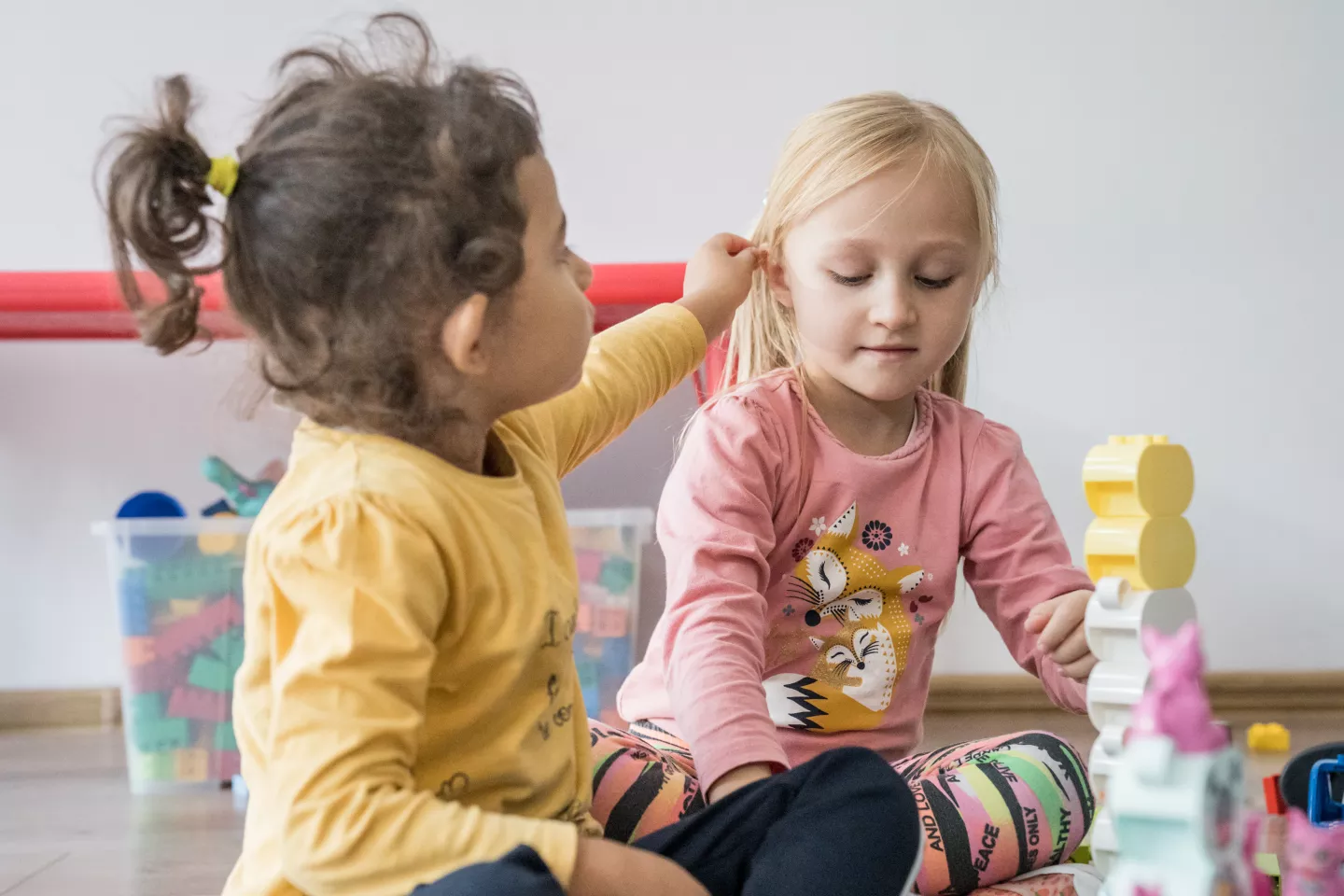 Dos ni&ntilde;as jugando. Una de ellas le est&aacute; poniendo el pelo por detr&aacute;s de una oreja a otra.