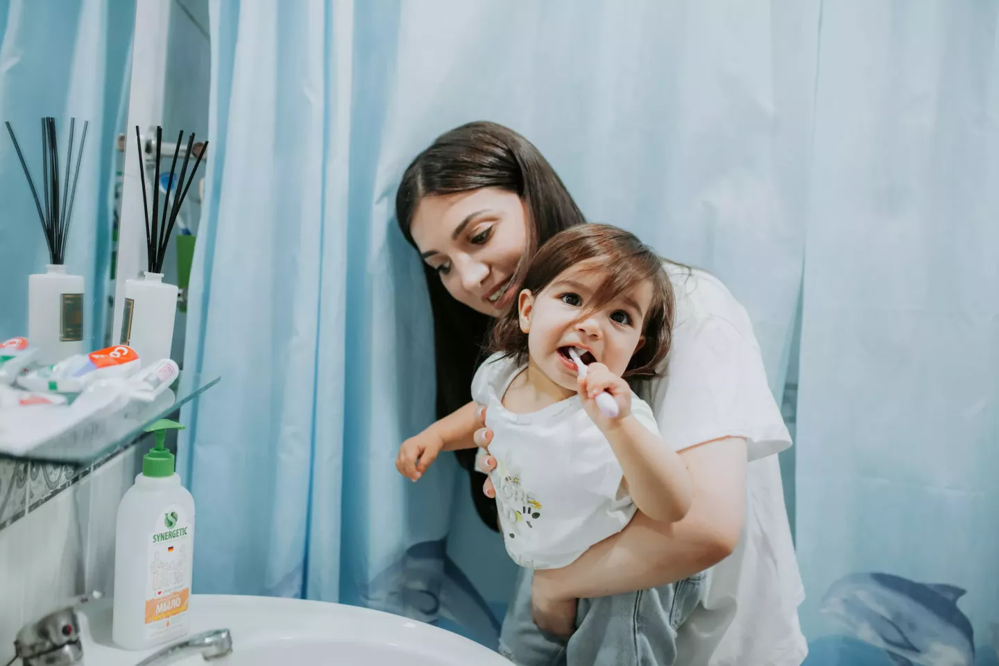 Mam&aacute; ayudando a su hija a lavarse los dientes