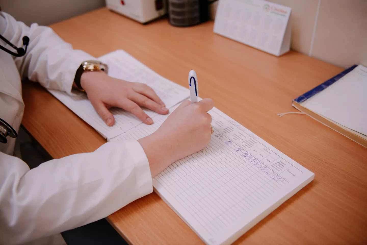 Mano sosteniendo una lapicera, escribiendo sobre un cuaderno.