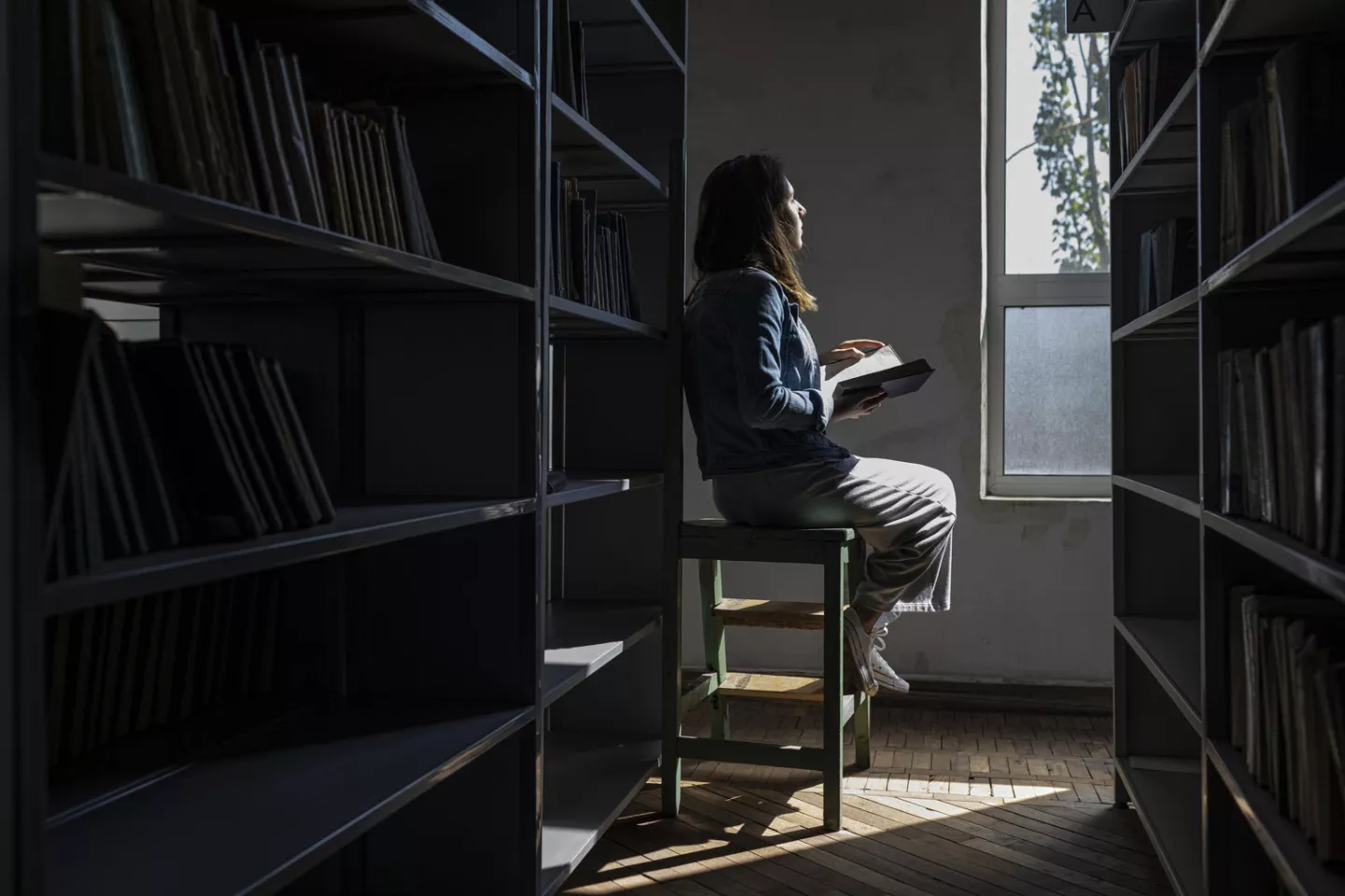 Adolescente sentada de espalda, a contra luz, mira por la ventana de una biblioteca