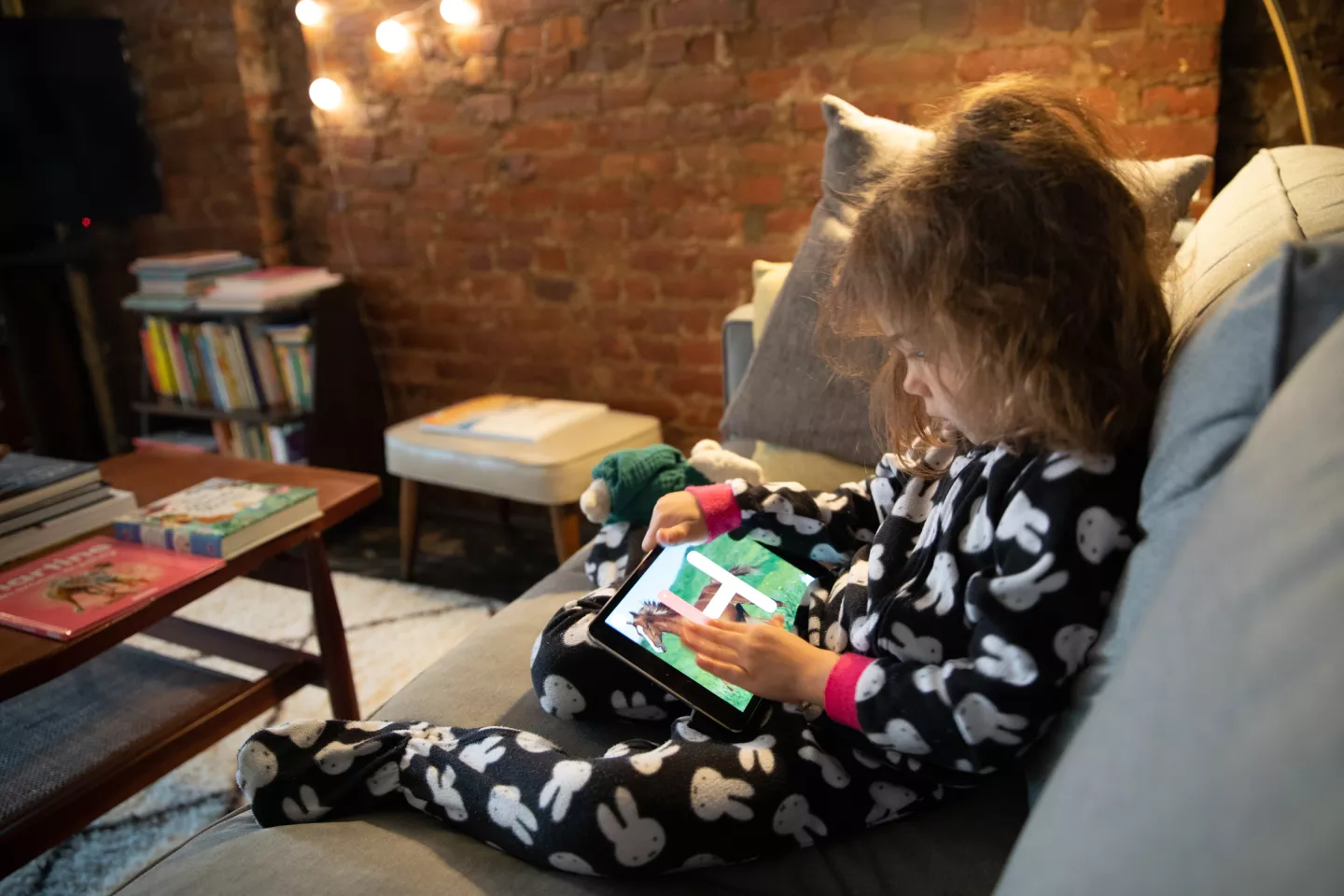 Ni&ntilde;a de cuatro a&ntilde;os, sentada en sill&oacute;n, jugando con tablet.